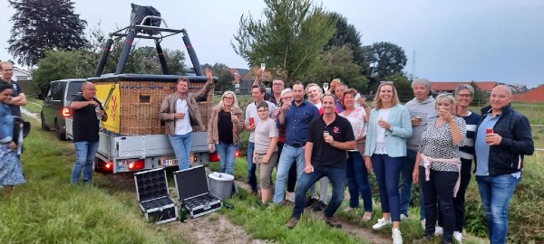 Passagers heureux portant un toast avec une coupe de champagne devant la nacelle après un vol en montgolfière au coucher du soleil.